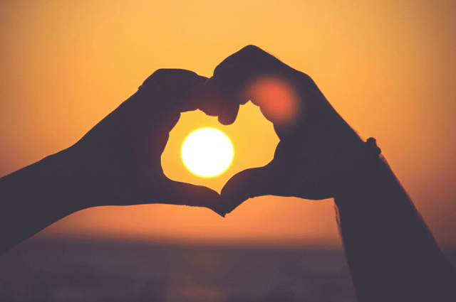 Hands make a heart shape, capturing a sunset