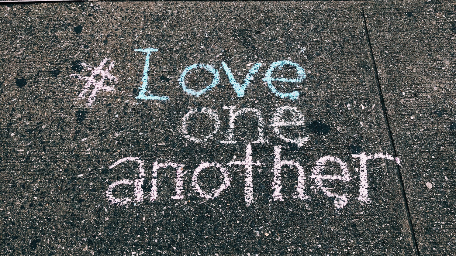 Image of a pavement with 'Love one another' written in chalk