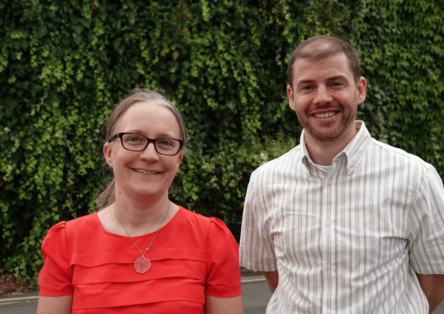 woman in red t-shirt, erica and man in short sleeve shirt, lee, stood in front of green bushes