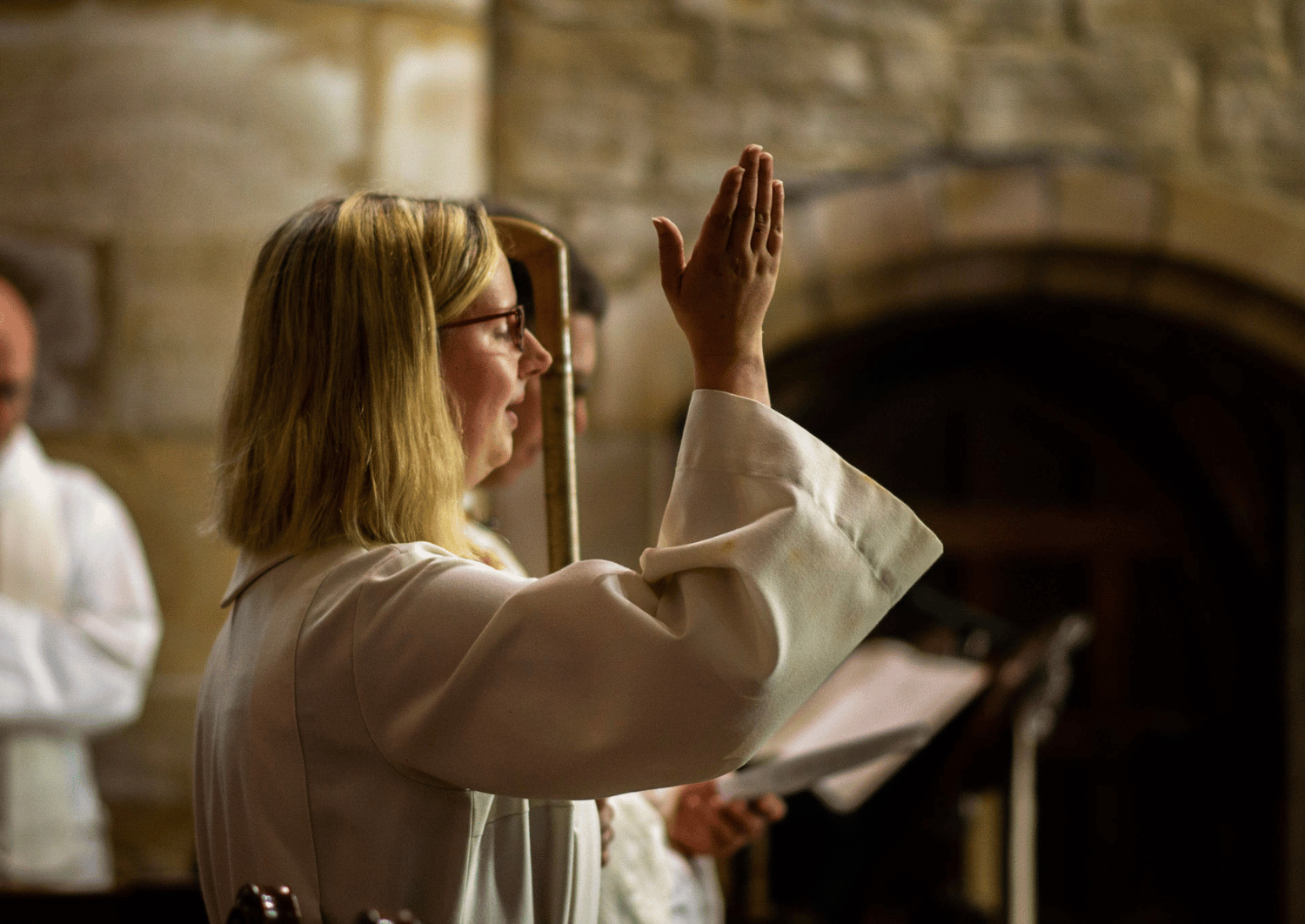 Image of female priest in white robe making the sign of the cross whilst holding a wooden staff