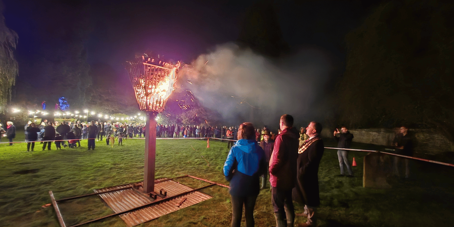 Fire lit in a beacon, spectators watching in the foreground and background