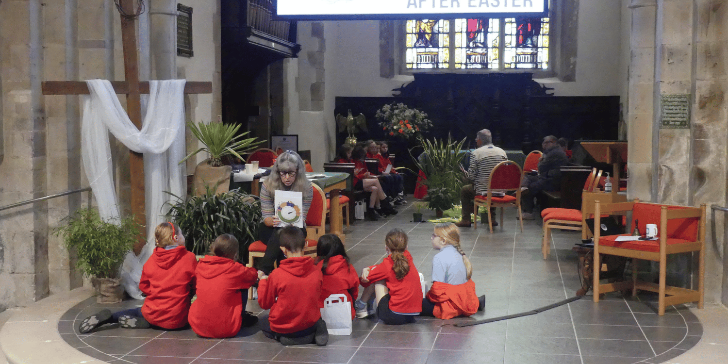 Image of school children listening to a story sat next to large wooden crucifix in church