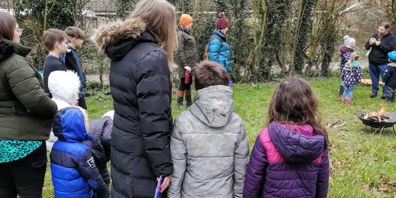 Children and adults stood outdoors around a firepit