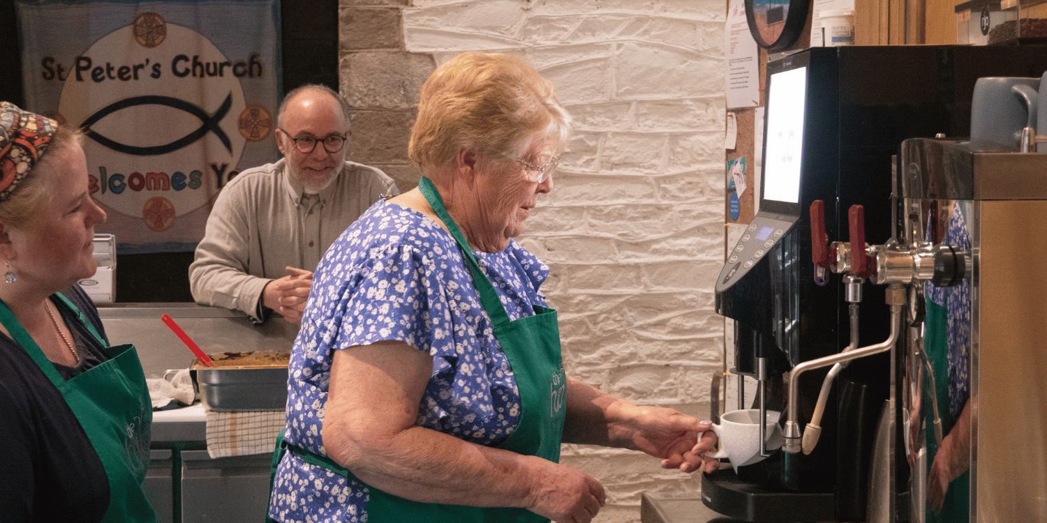 Volunteer wearing apron making cup of coffee using coffee machine at The Hub in Peterchurch Herefordshire