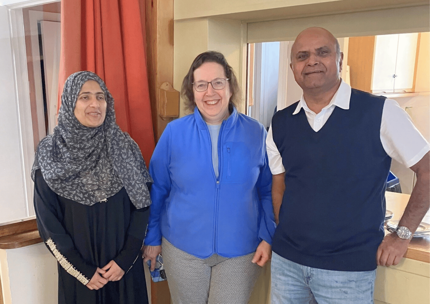a woman wearing a headscalf stood next to a woman wearing a blue fleec top and a man, all smiling