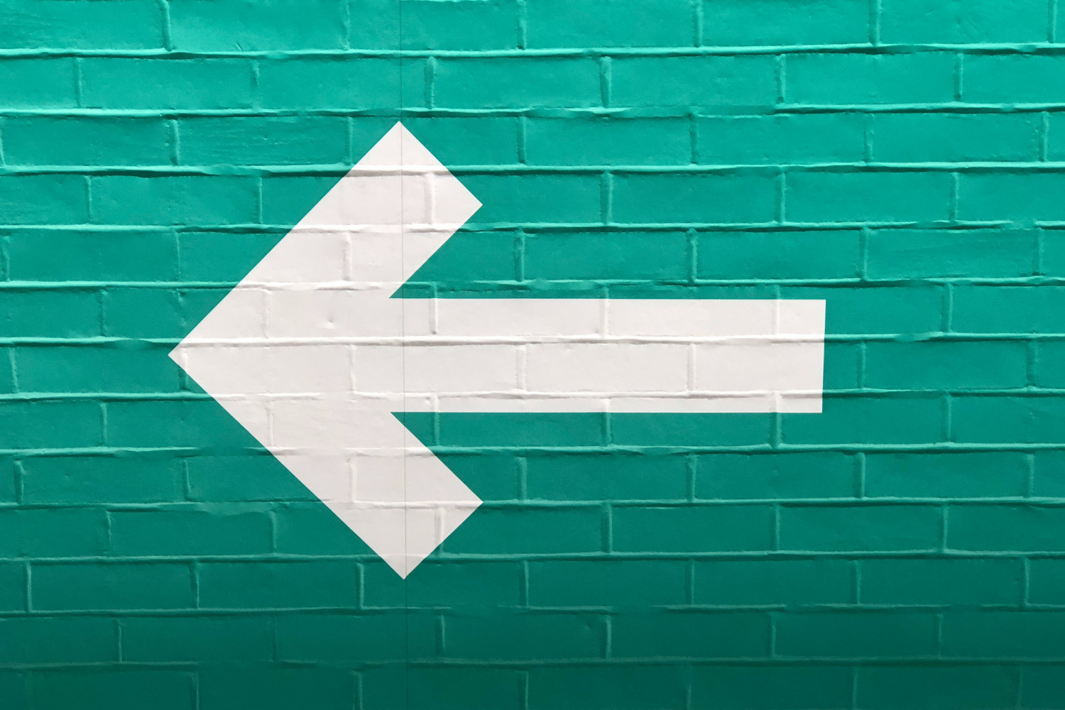 Image of a left-pointing, white arrow on a bright green brick wall