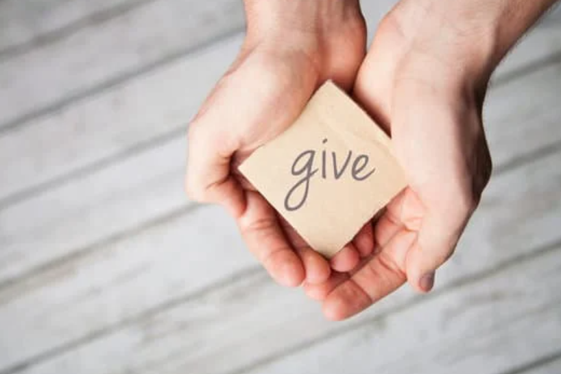 Image of a hands cupping a post it notes with the word 'give' written on it