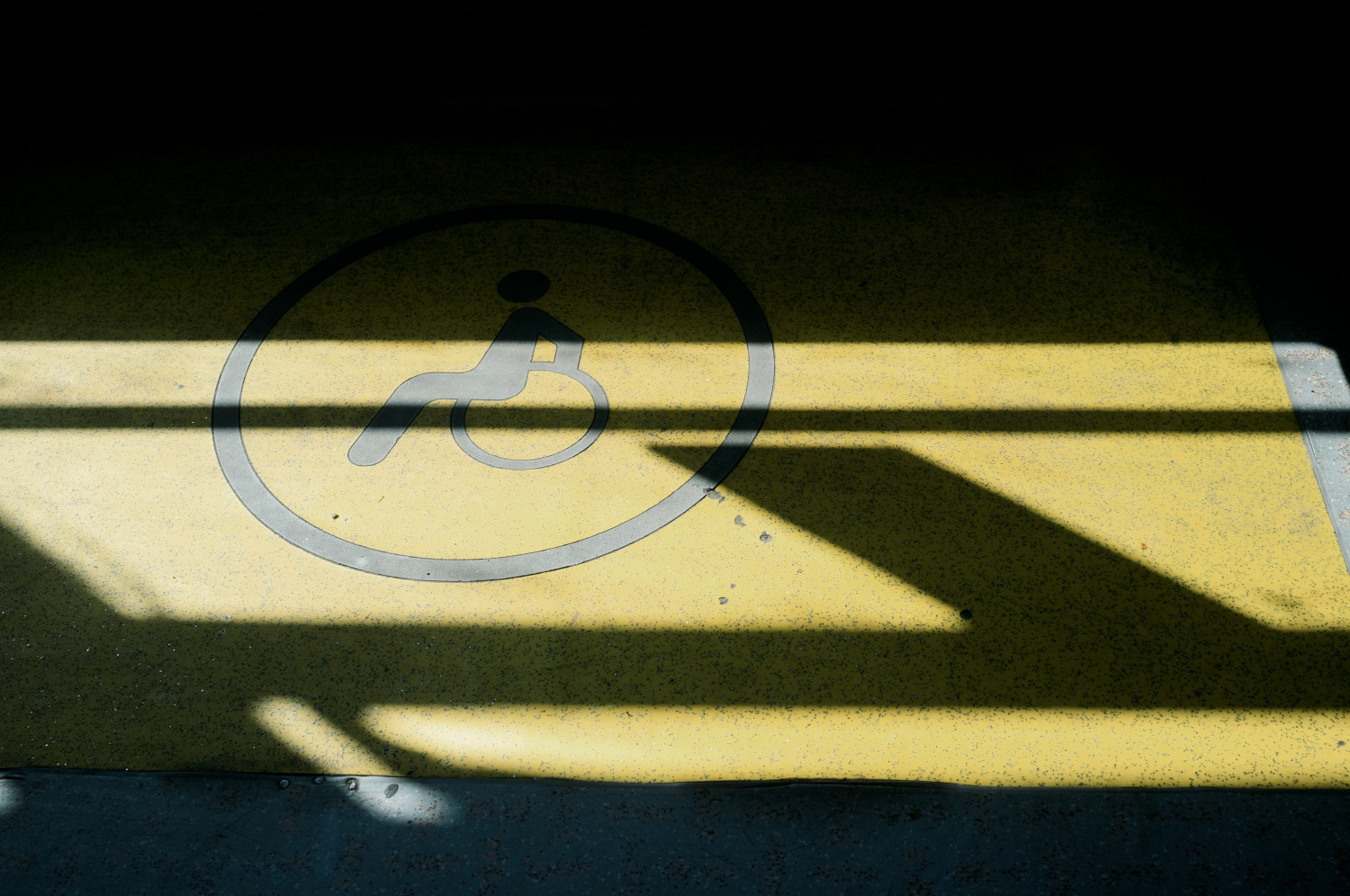 Image of a sun-lit concrete floor with a bright yellow painted disability symbol