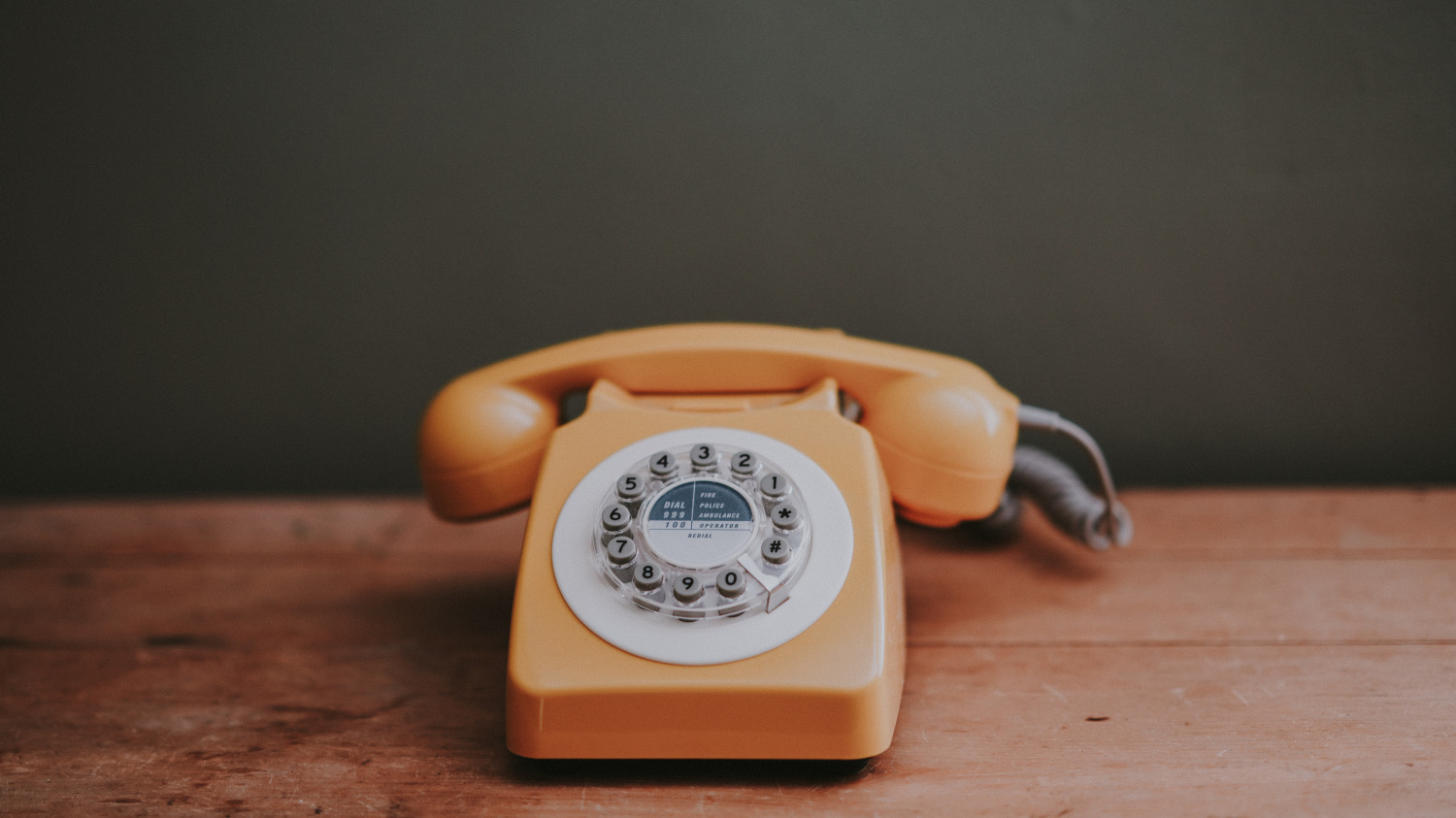 Image of an orange rotary phone on a wooden desk