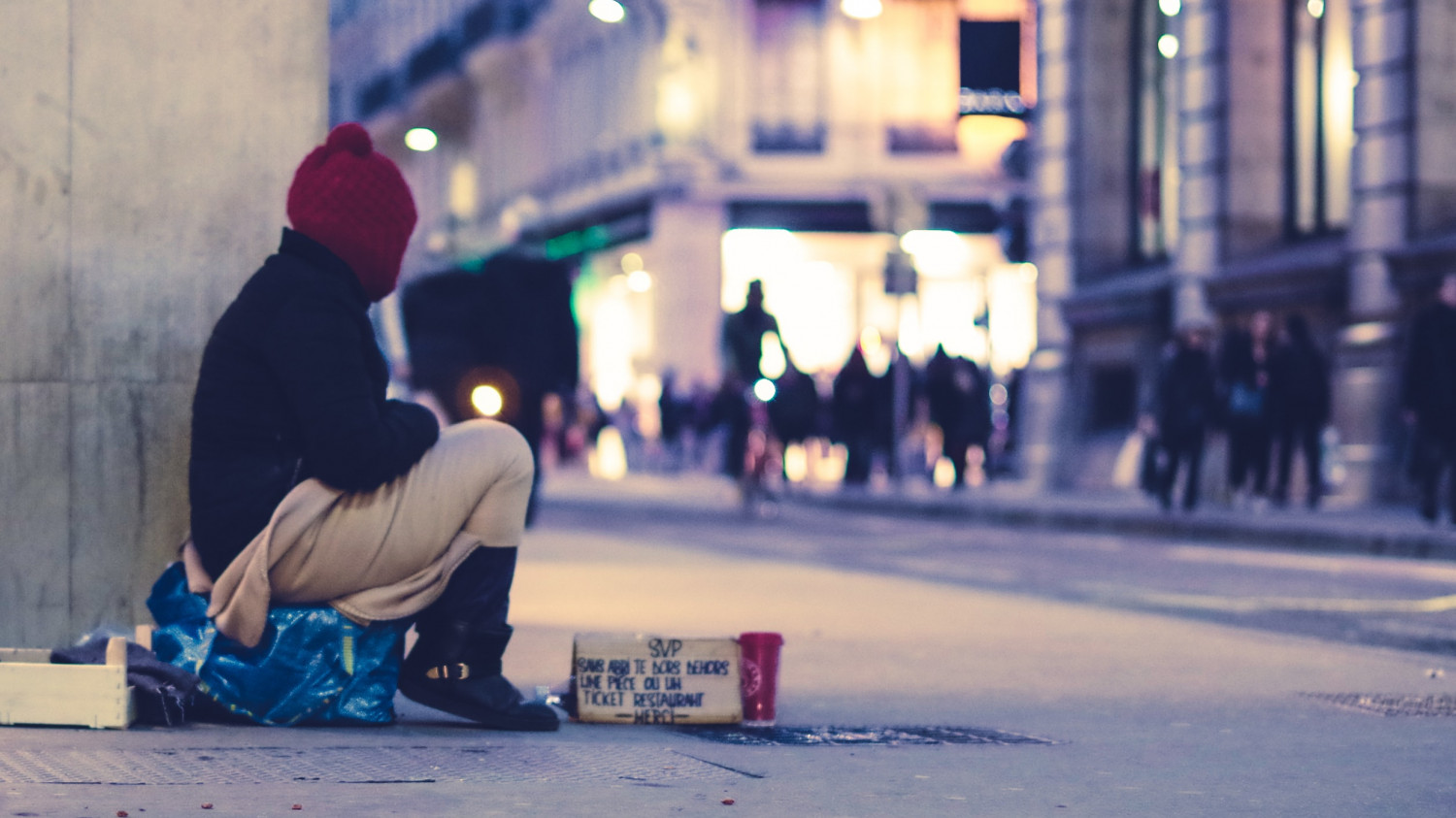 Image of a homeless woman seated on a cardboard box in a busy highstreet
