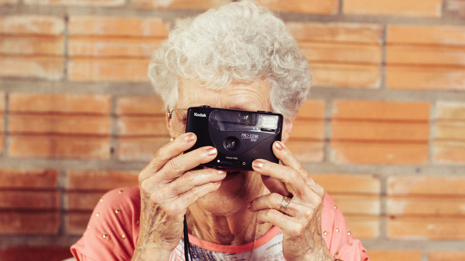 Image of an elderly woman with a camera held up to her face taking a photo