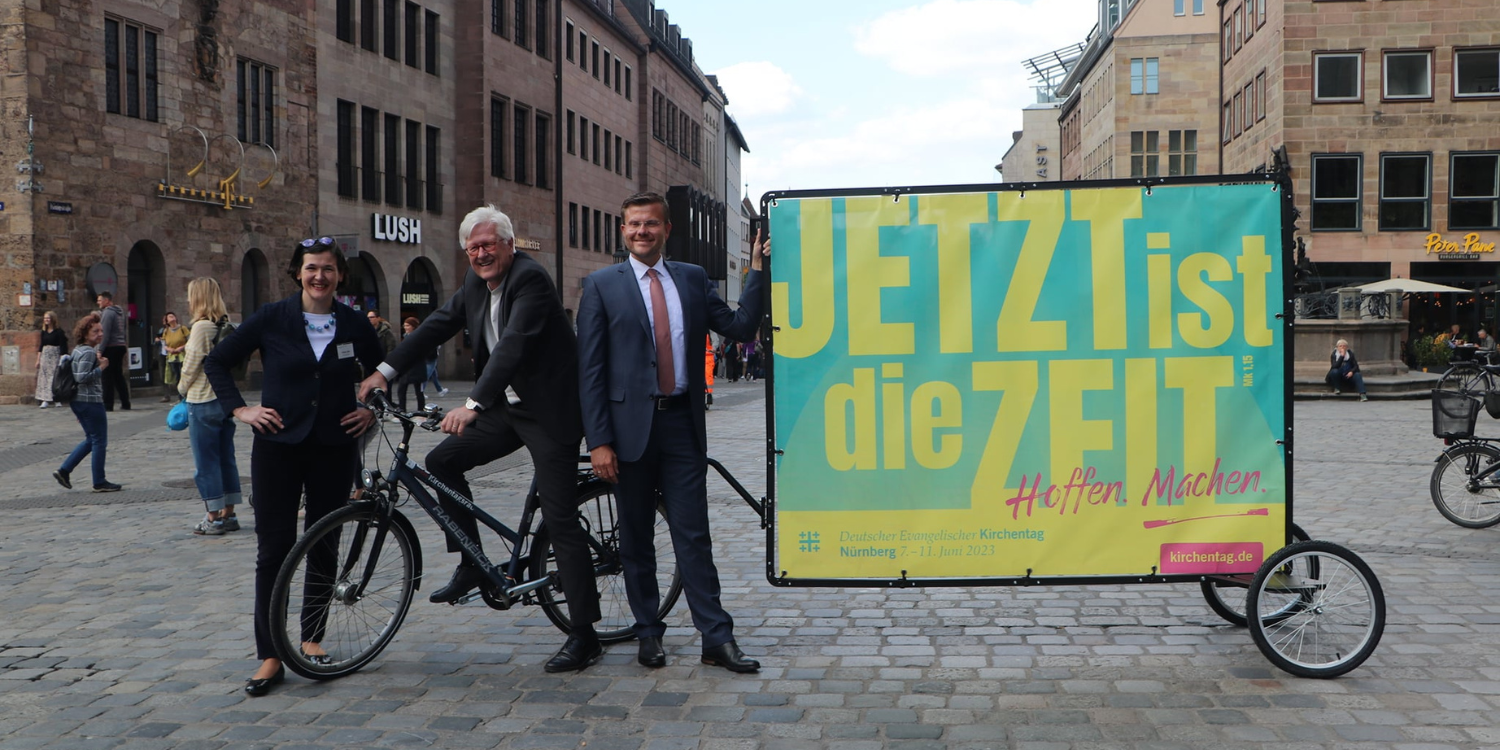Vicar pulling an advert on the back of a bicycle for Kirchentag 2023